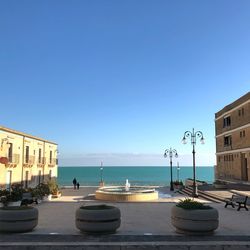 Boats on sea by buildings against clear blue sky