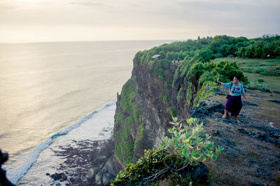 Mature man photographing sea while standing on mountain during sunset