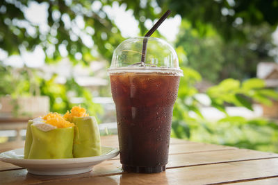 Close-up of drink and food on table against trees