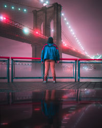 Rear view of man standing against illuminated brooklyn bridge at night