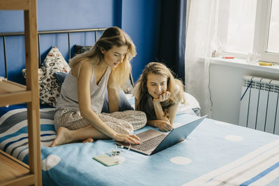 Fun young beautiful women twins work at home behind a laptop