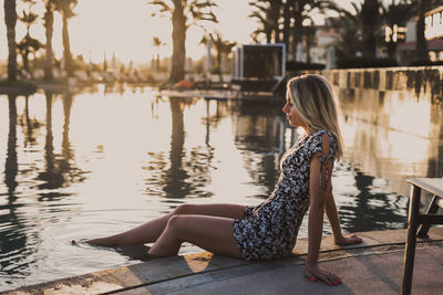 Side view of young woman sitting by lake