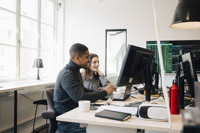 Smiling software programmers discussing over laptop on desk in office