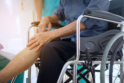 Midsection of patient holding leg while sitting on wheel chair