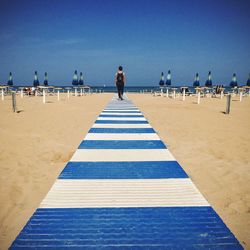 Full length rear view of woman walking on striped pier at beach