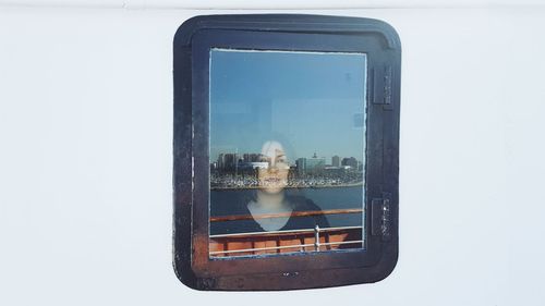 Woman seen through ship window with reflection of city and sea