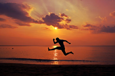 Side view of man with arms outstretched jumping at beach at sunset