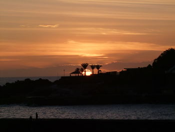 Silhouette people on shore against sky during sunset