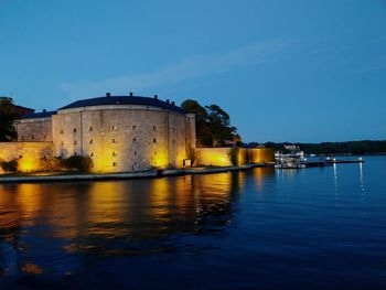 Vaxholm fortress by lake in city at dusk