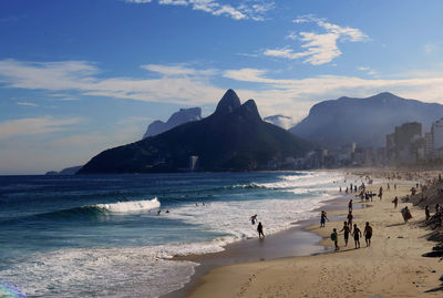 People walking at beach by mountains against sky