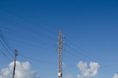 Low angle view of electricity pylon against blue sky