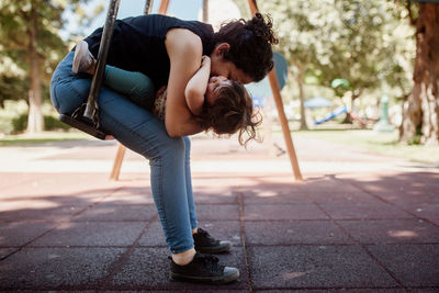 Mother embracing daughter while sitting on swing