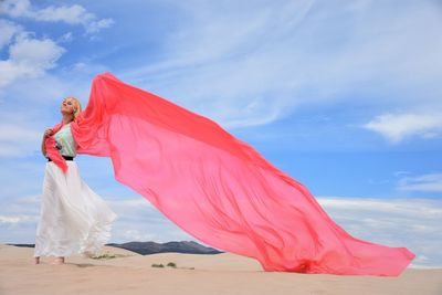 Mid adult woman with coral dupatta at desert against sky