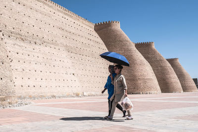 Woman with umbrella walking on street against clear sky