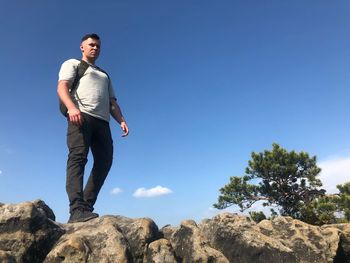 Man standing on rock against blue sky