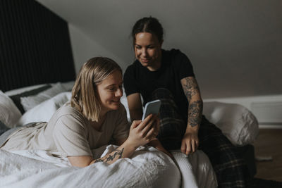 Homosexual female couple sitting on bed and looking at cell phone