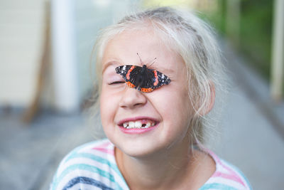 A beautiful black butterfly with orange spots sits on face of a cheerful blonde  girl 7-8 years.