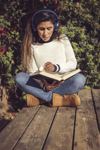 Latina woman, sitting outdoors listening to music and reading