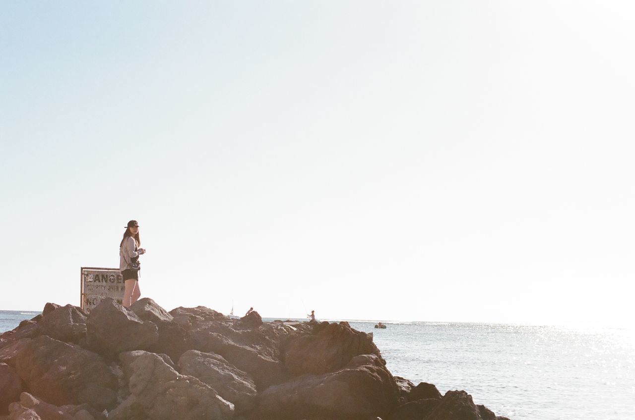 YOUNG WOMAN SITTING ON ROCK AGAINST SEA