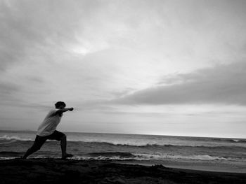 Side view of man running at beach against cloudy sky