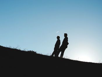 Low angle view of silhouette men walking on sand against clear sky