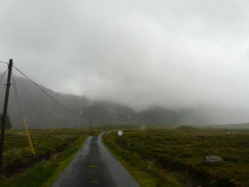 Road amidst landscape against sky during foggy weather