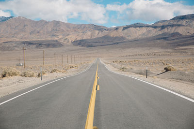 Empty road by mountains against sky