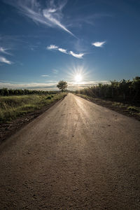 Empty road amidst field against sky