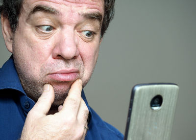 Close-up of confused man looking at mobile phone