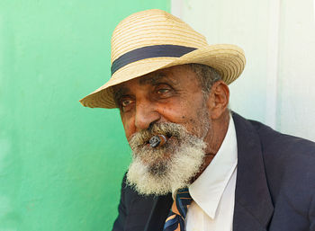 Portrait of man smoking cigar while sitting against wall