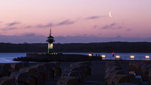 Lighthouse by sea against sky at sunset