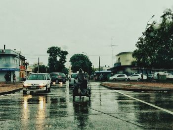 Cars on wet street against sky during monsoon