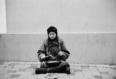 Portrait of woman sitting on footpath against wall