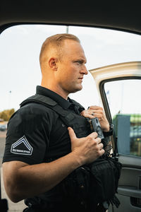 White male police officer standing outside of vehicle to investigate a situation