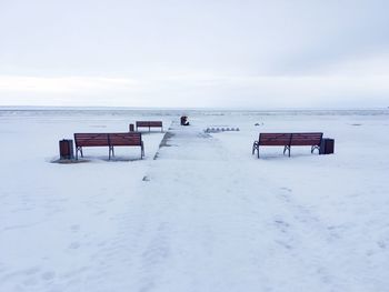 Empty bench on snow covered land against sky