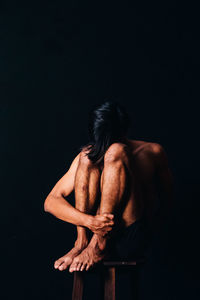 Full length of depressed man sitting on stool against black background