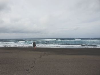 Rear view of woman walking at beach against sky