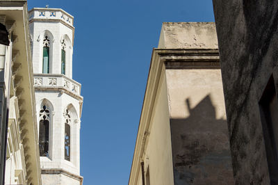 Low angle view of cross amidst buildings against clear blue sky