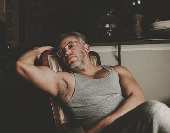 Thoughtful muscular mature man sitting on chair at home