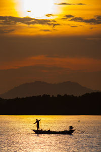 Silhouette people in boat against sky during sunset