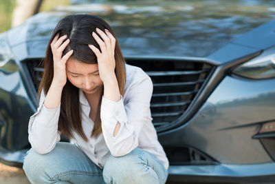 Tensed woman with head in hands crouching against car
