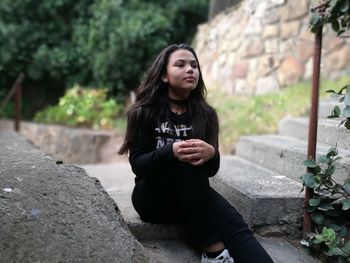 Woman looking away while sitting on steps outdoors