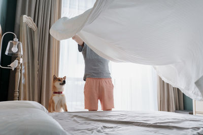 Young man and his funny dog are putting the bedding cover or mattress pad on the bed