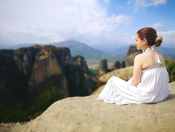 Rear view of woman sitting on rock against sky