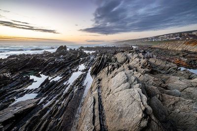 Scenic view of sea and rock pools against sky during sunset with stone audience