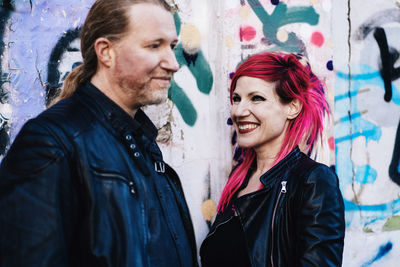 Smiling man and woman standing against graffiti wall