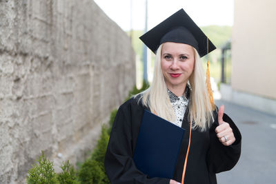 Young woman wearing graduation gown standing against trees