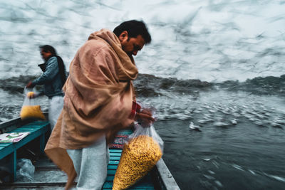 Side view of men feeding birds in river from boat