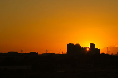 Silhouette buildings against orange sky during sunset