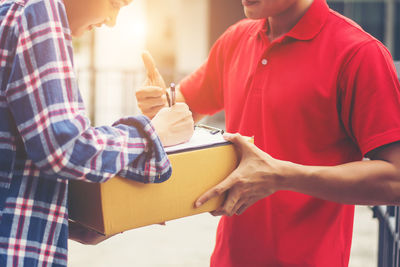 Midsection of female customer signing receipt while receiving package from delivery man outdoors